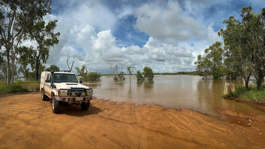 A police car parked at the edge of a flooded road in the outback