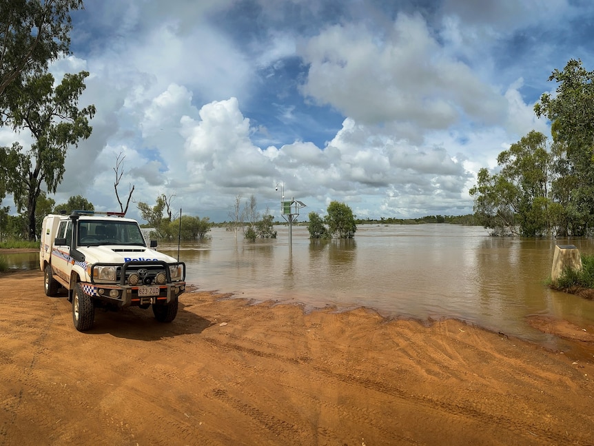 A police car parked at the edge of a flooded road in the outback