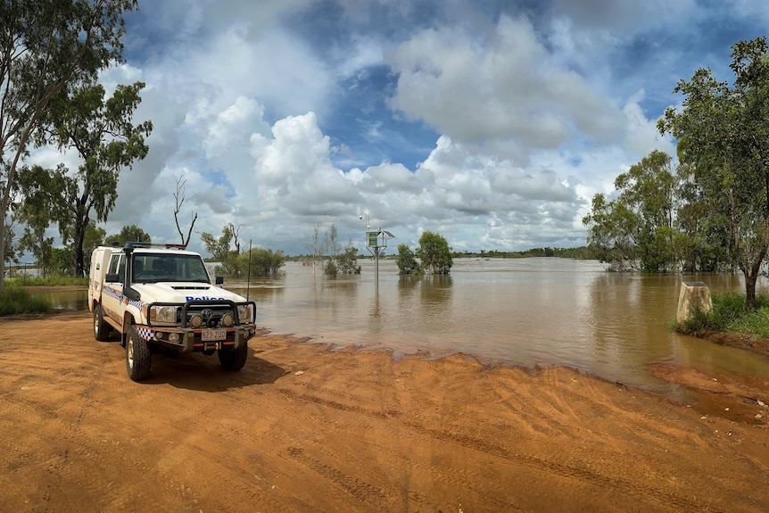 A police car parked at the edge of a flooded road in the outback