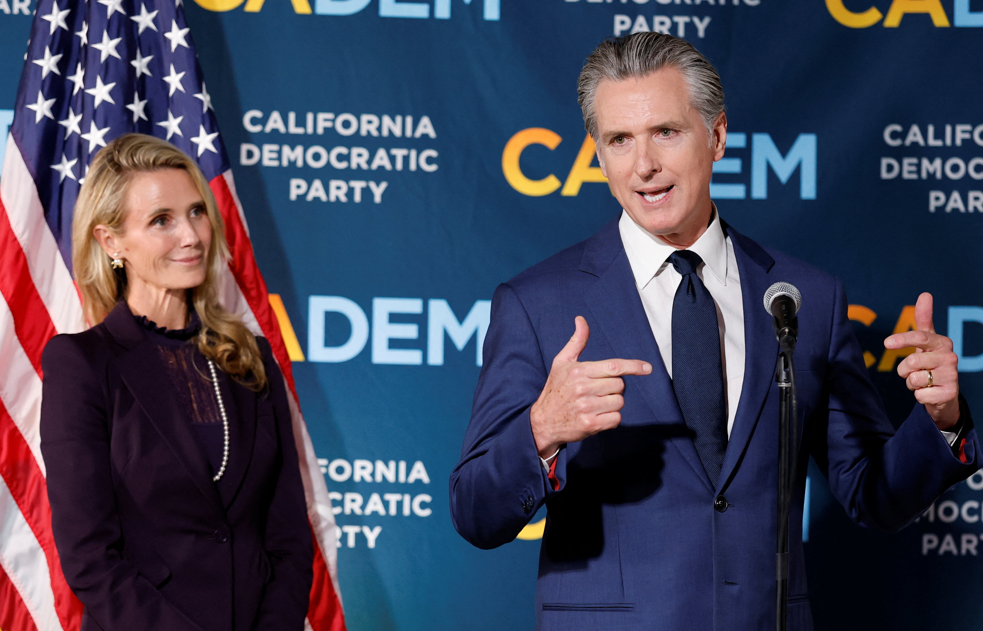 A woman standing next to a man delivering a speech 