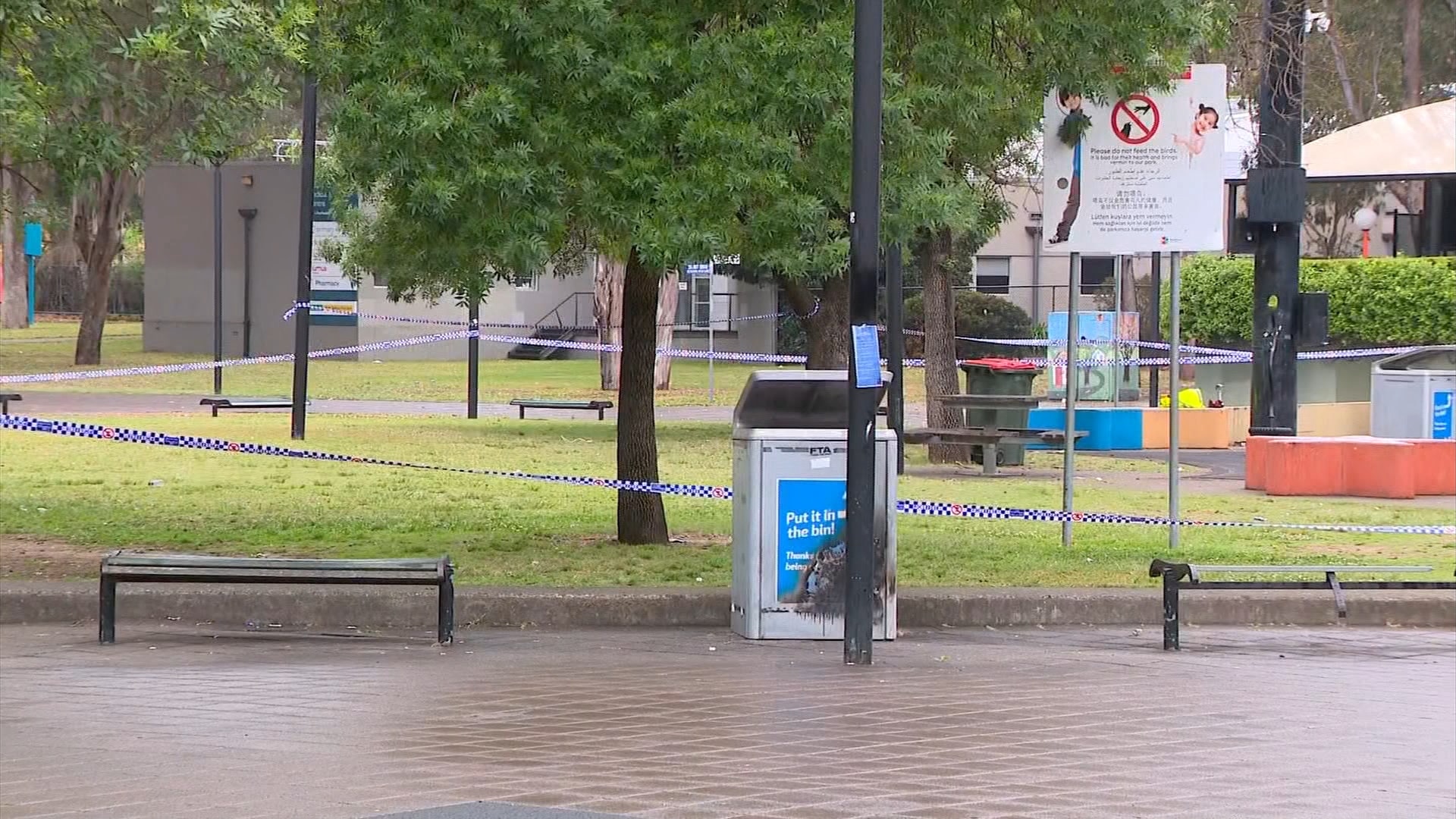 A park area next to some walkway streets, with police tape around it.