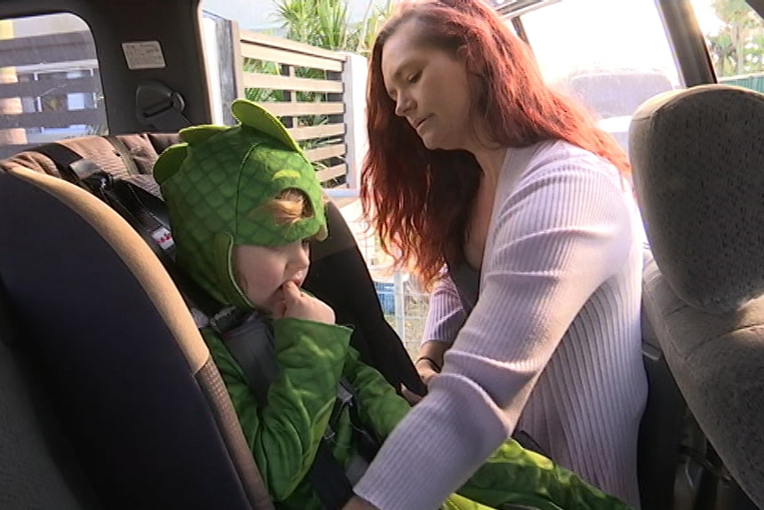 Jenna Davies puts her daughter Paige, dressed in a gecko costume, in a child seat in her car