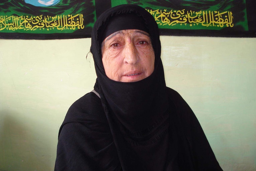 A woman in black hijab, crying, looks at the camera.