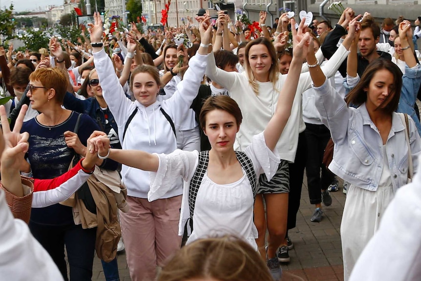 Women dressed in white hold hands while marching