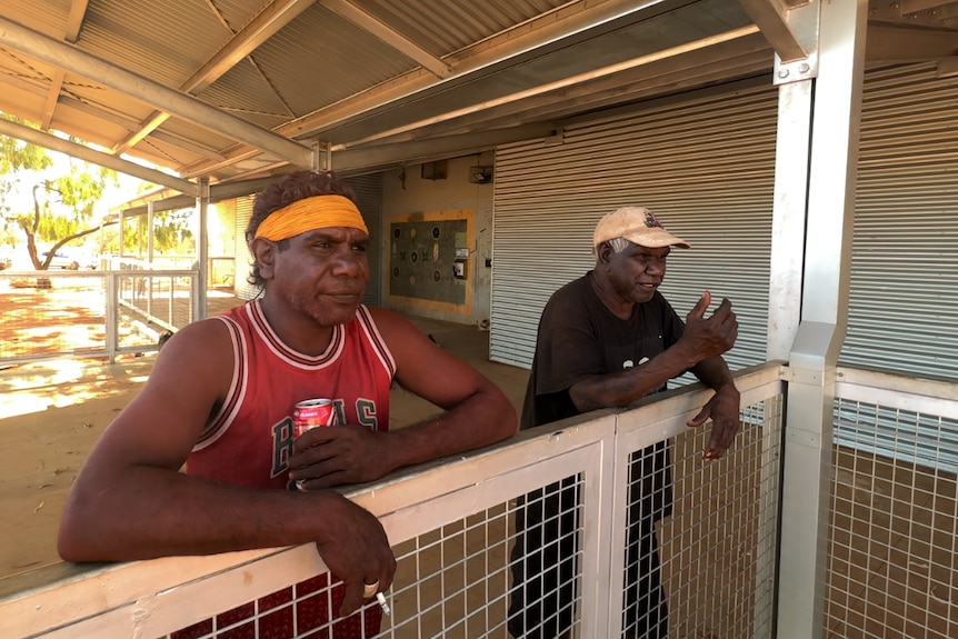 Two men lean on a rail.