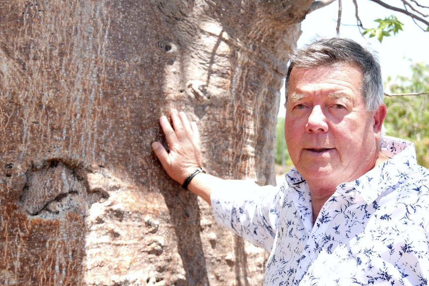 A man stands leaning against a tree 