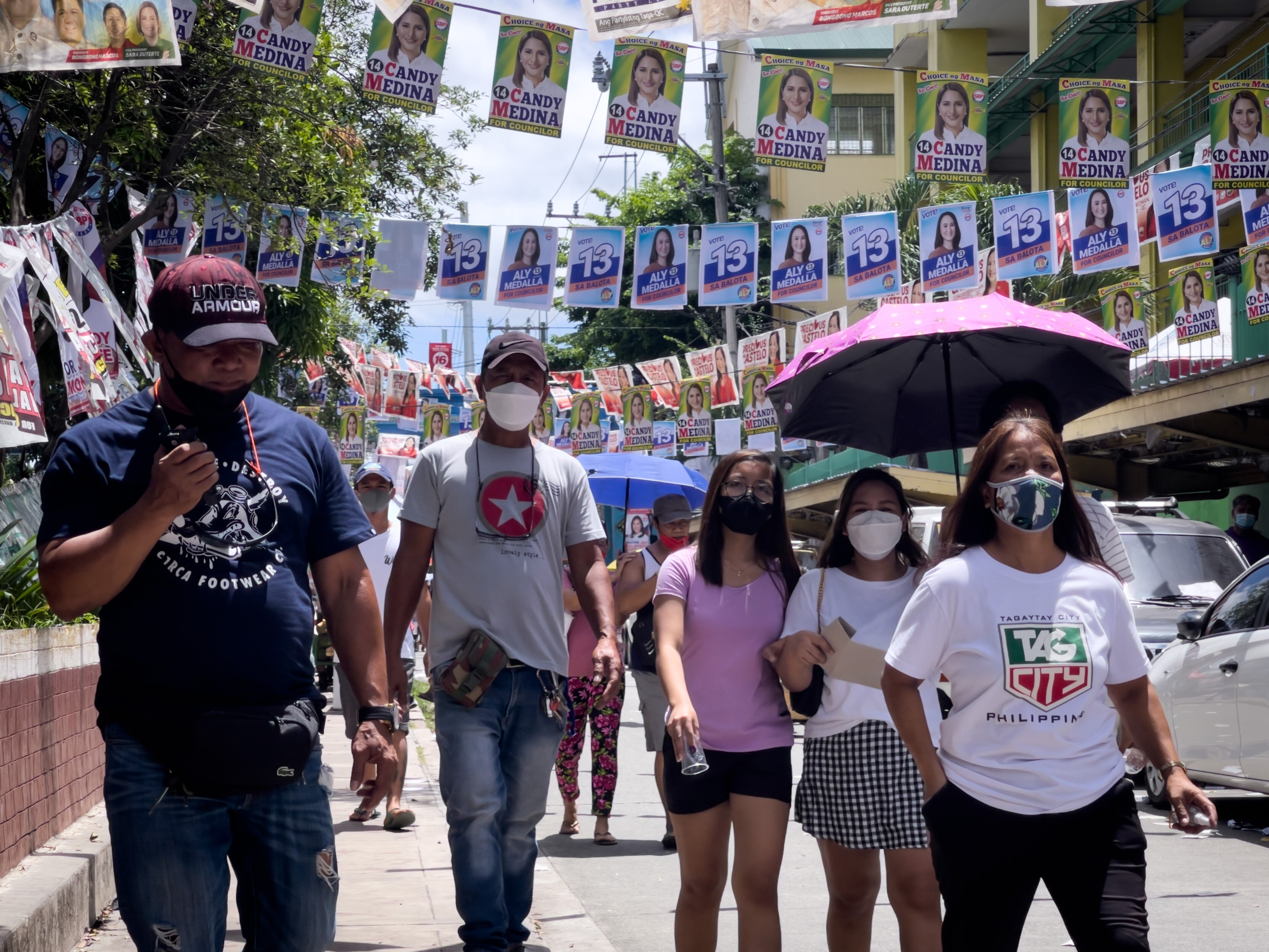 Groups of people walk down the street, above them there are strings of election campaign posters