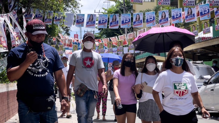 Groups of people walk down the street, above them there are strings of election campaign posters