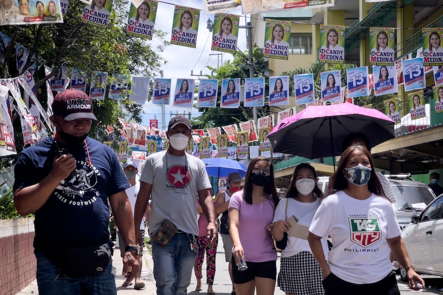 Groups of people walk down the street, above them there are strings of election campaign posters