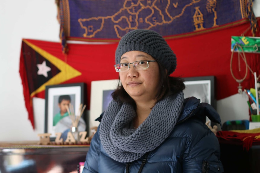 A woman sits in front of an East Timor flag.