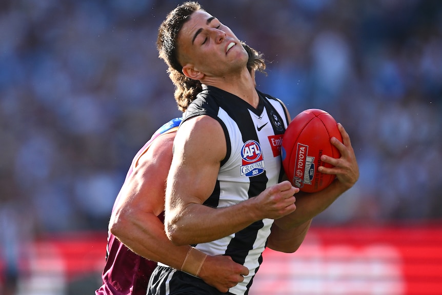 A Collingwood AFL player is tackled while being holding the ball in the grand final.