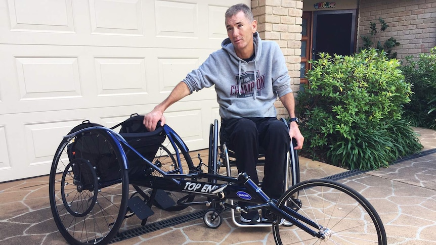 A man in a wheel chair sits next to his racing wheel chair.