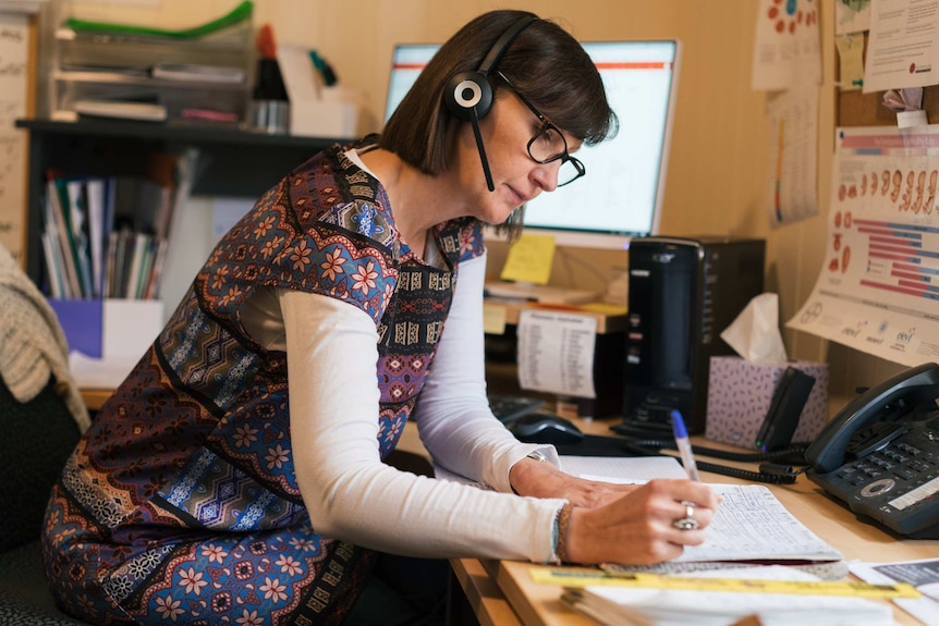 Counsellor Michelle Reynolds sits at her desk wearing a phone headset while speaking to a woman enquiring about an abortion.