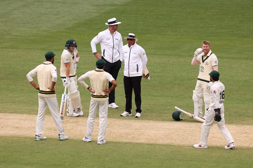 Pakistan and Australia players speak to umpires during a delay on the MCG pitch.
