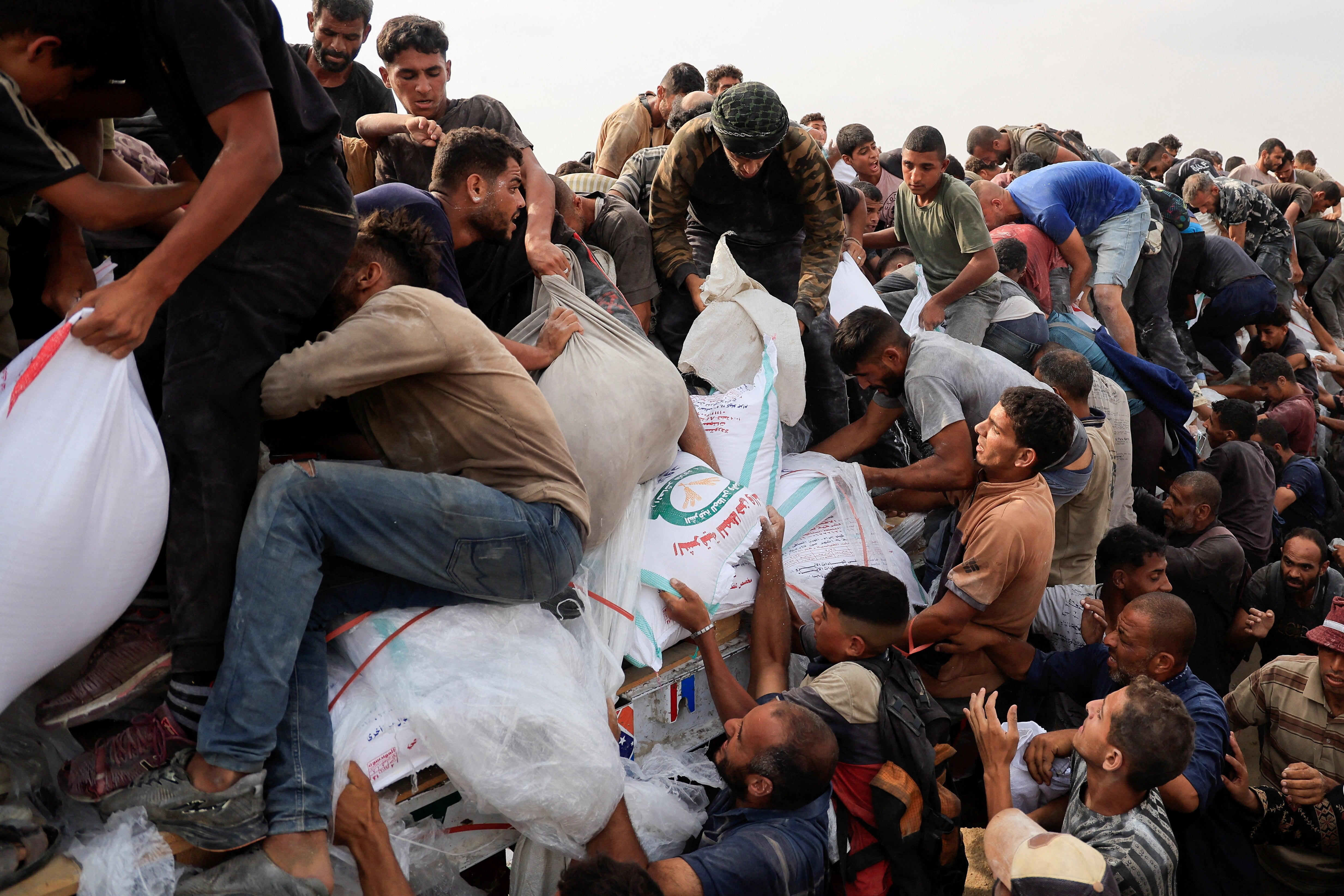 A crowd of people stepping over each other to grab white sacks filled with aid. 