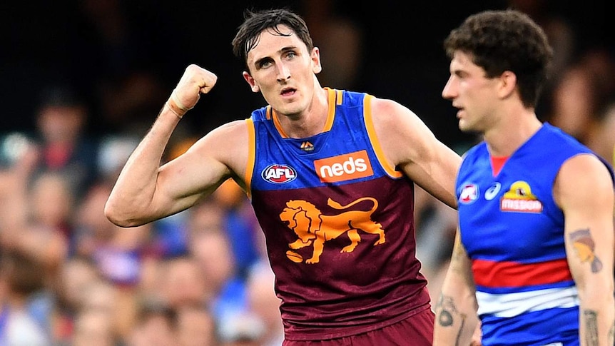 An AFL player pumps his fist at the crowd in celebration after kicking a goal.