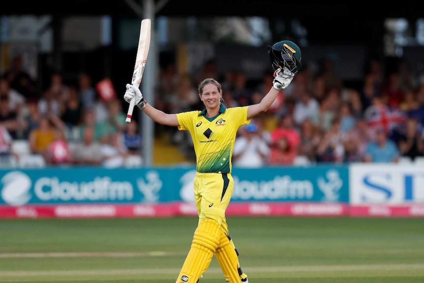 A cricketer raises her bat in one hand and her helmet in the other as he celebrates her century.