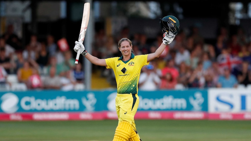 A cricketer raises her bat in one hand and her helmet in the other as he celebrates her century.