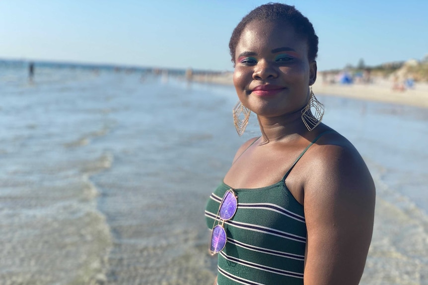 A woman smiles while wading in the swallows at the beach.