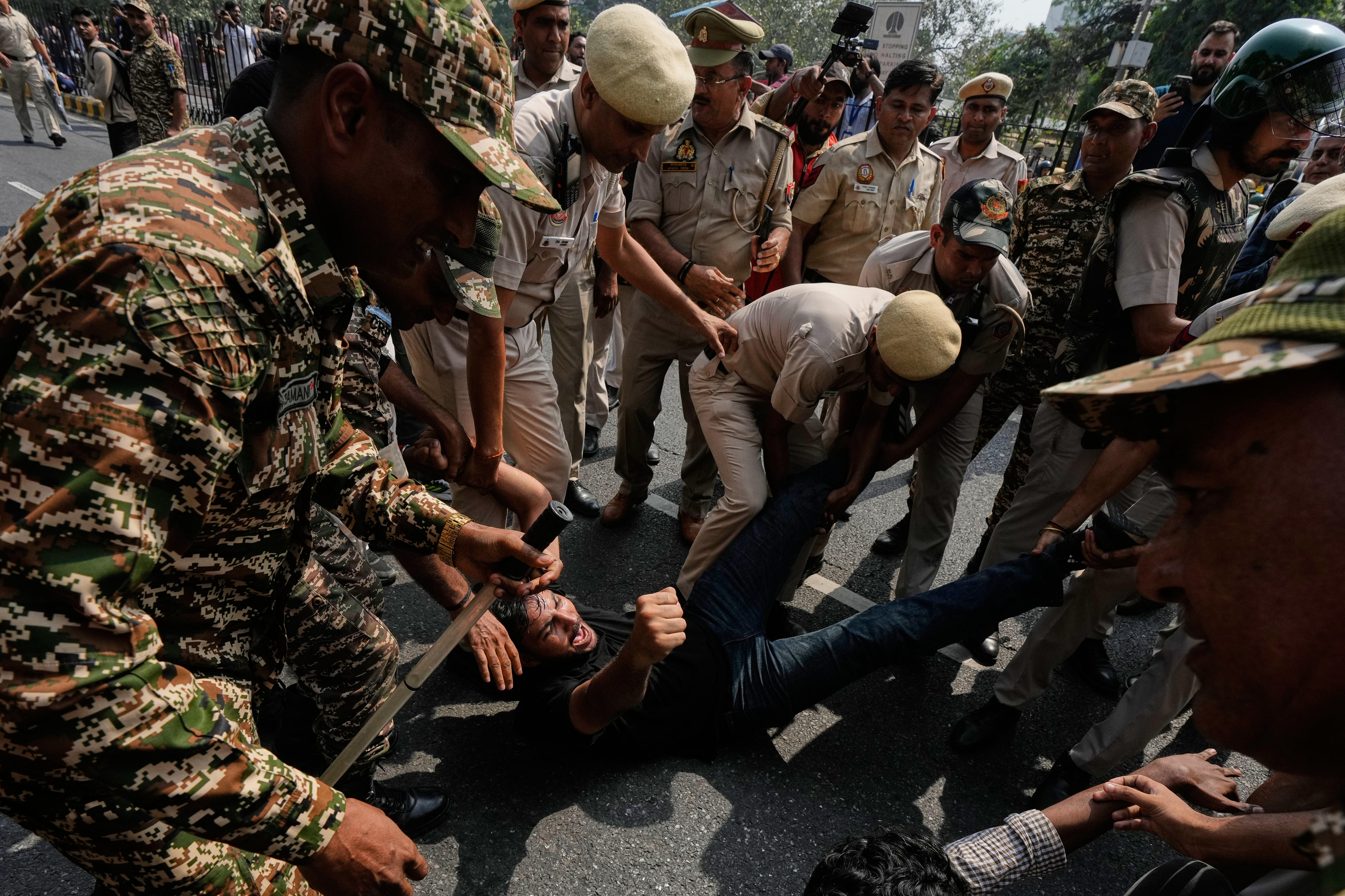 A young male protester lies on the ground, surrounded by police who are pulling him from his legs