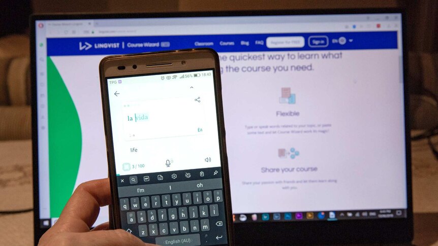 A phone is held in front of a computer screen showing the Lingvist app.