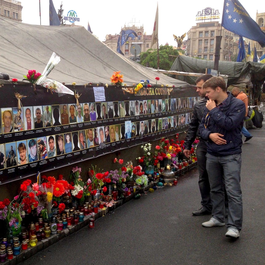 Passersby look at wall of photos of fallen activists in a square in Kiev, Ukraine.