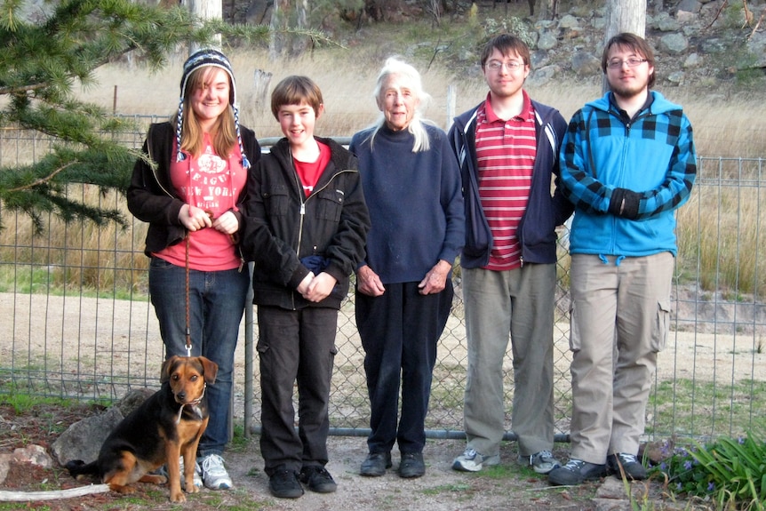 A woman with silver hair poses for a photo flanked by her four grandchildren, one of whom has a small dog.