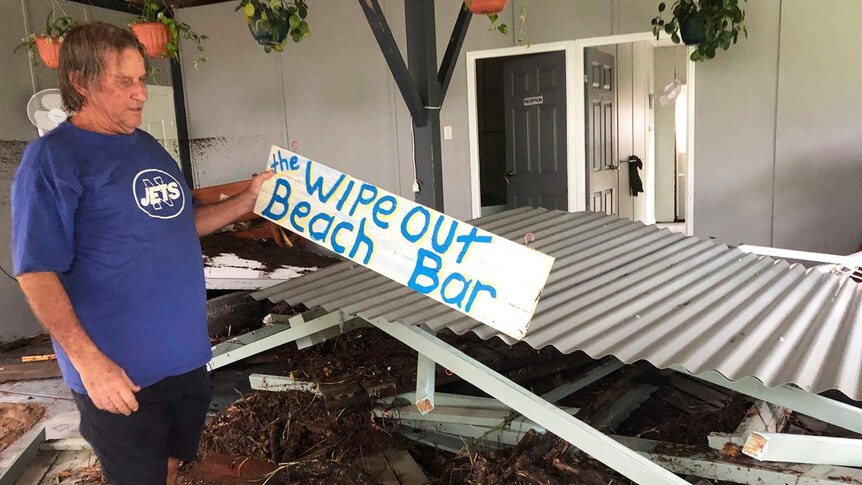 Resident Roger Goodwin holds a sign 'The Wipeout Beach Bar' among his flooded-ravaged home at Bluewater.