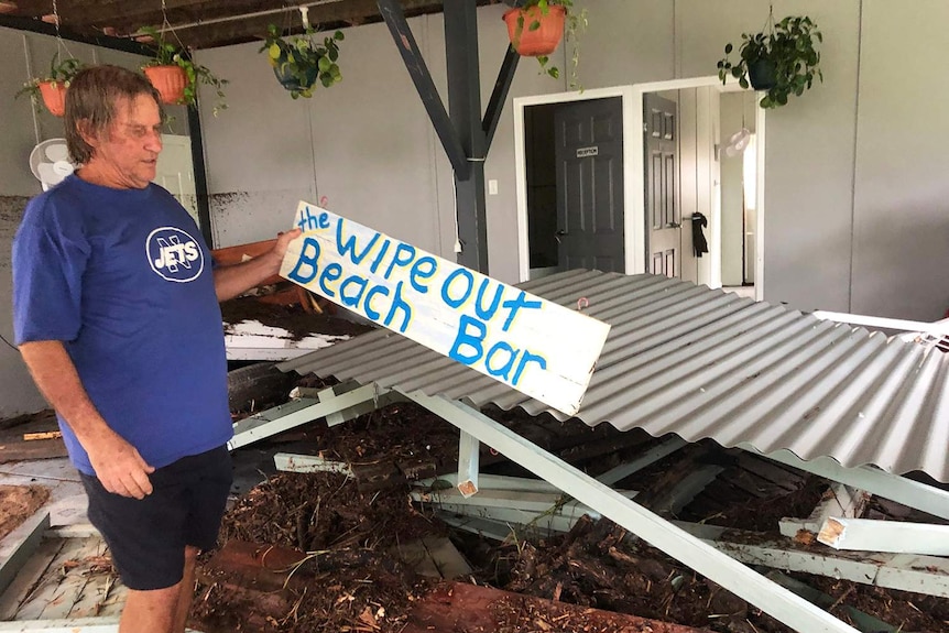 Resident Roger Goodwin holds a sign 'The Wipeout Beach Bar' among his flooded-ravaged home at Bluewater.