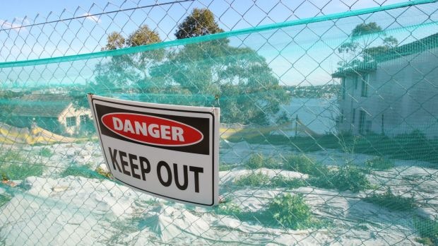A 'Danger Keep Out' sign against a fence in front of a waterfront block