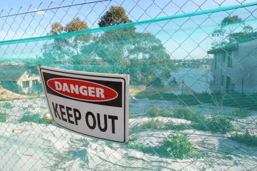 A 'Danger Keep Out' sign against a fence in front of a waterfront block