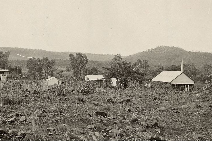 A black and white landscape photos of old buildings scattered in bush and rolling hills.
