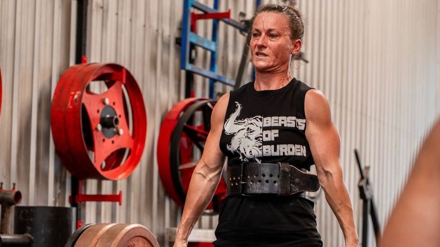 Athelia Soley's veins bulge in her forehead and arms as she lifts a weight in a gym.