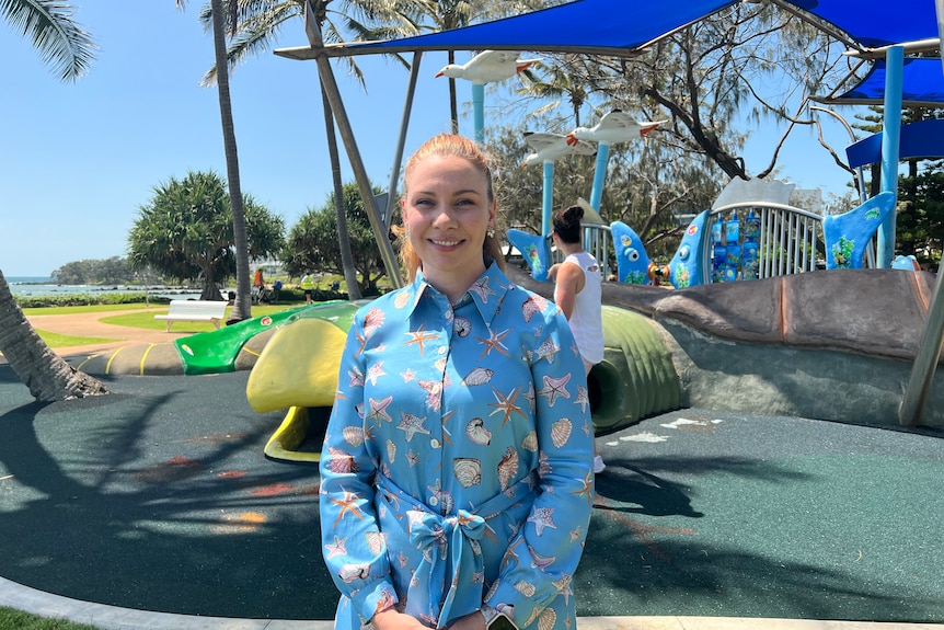 A woman in a blue dress stands in front of a turtle playground. 