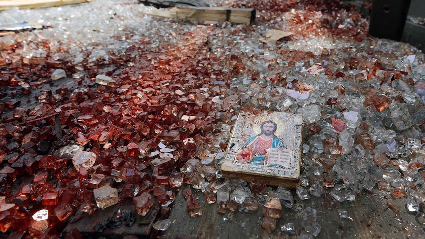 A blood-stained icon of Jesus lies among blood-soaked shattered glass in the back of a truck.