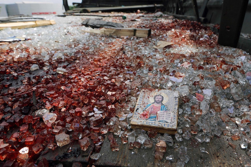 A blood-stained icon of Jesus lies among blood-soaked shattered glass in the back of a truck.