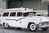 An old paddy wagon car with the ambulance logo, a siren and North Eastern Victoria District Ambulance Service on the side.