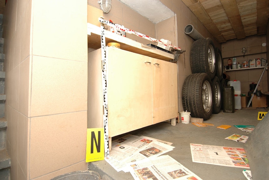 A corner of a basement or workshop with some stacked car wheels and simple wooden cupboards.