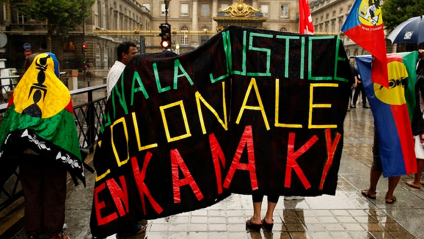 French police stand by as demonstrators holding New Caledonian 'Kanak' flags protest outside of the Paris court house