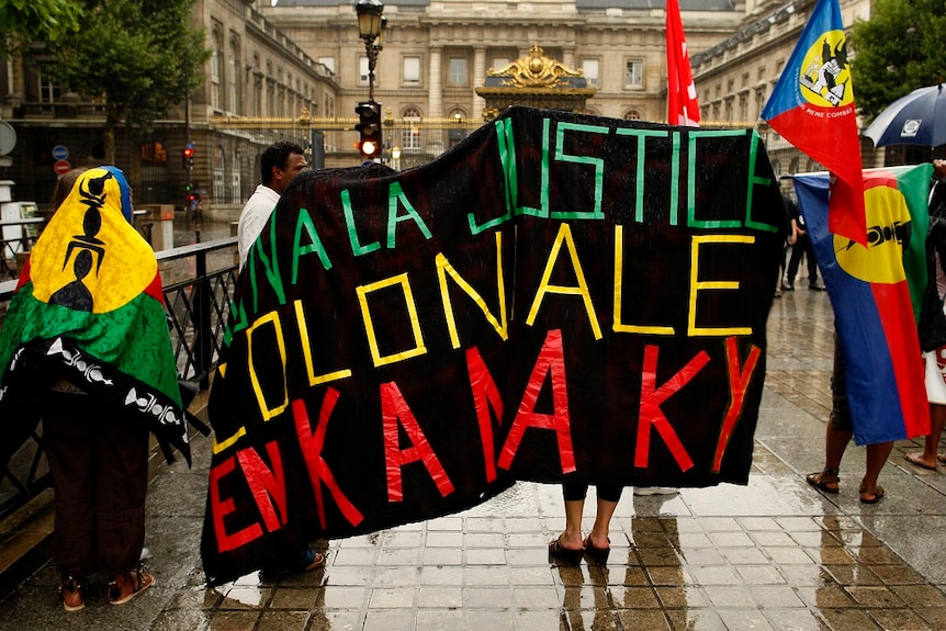 French police stand by as demonstrators holding New Caledonian 'Kanak' flags protest outside of the Paris court house