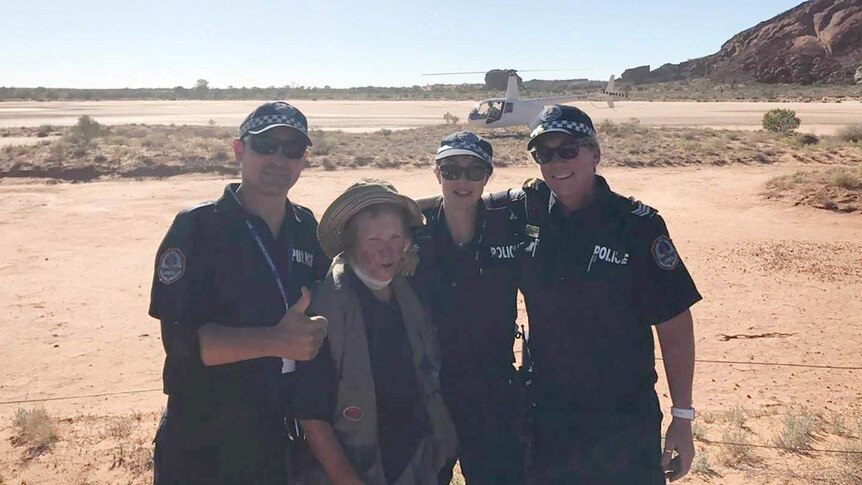 Rescued bushwalker Rose stands with three police officers and a helicopter in the background.
