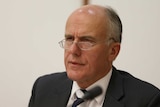 Eric Abetz, wearing a black suit with a white shirt and black and white striped tie, stares intently with a furrowed brow.