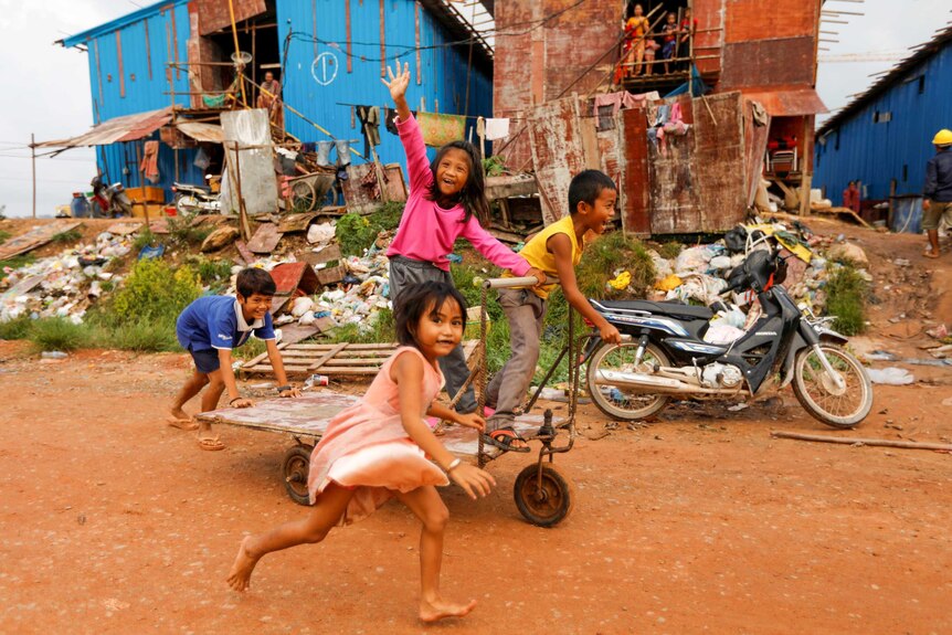A group of Cambodian children smile for the camera while running through a village
