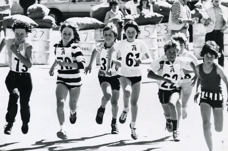 Black and white photo of children running with numbers on bibs at the front of their shirts.