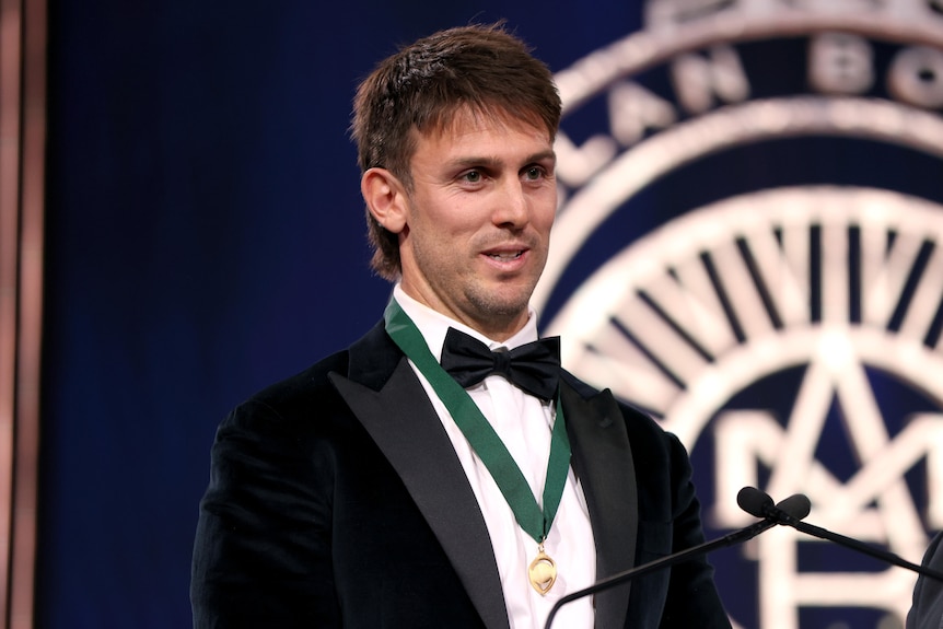An Australian cricketer smiles on stage as he wears a medal around his neck.