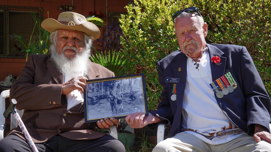 Two veterans sit, holding a framed photo