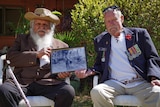 Two veterans sit, holding a framed photo
