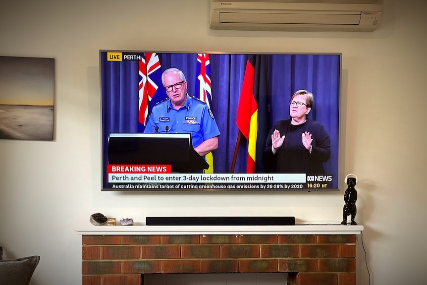 A TV screen in a living room broadcasting a COVID-19 press conference