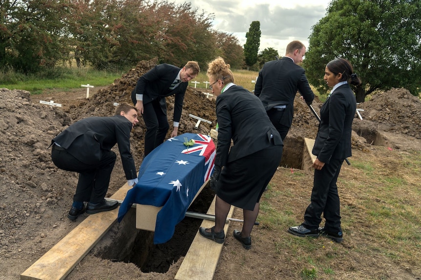A coffin wrapped in the Australian flag is lowered into the ground.