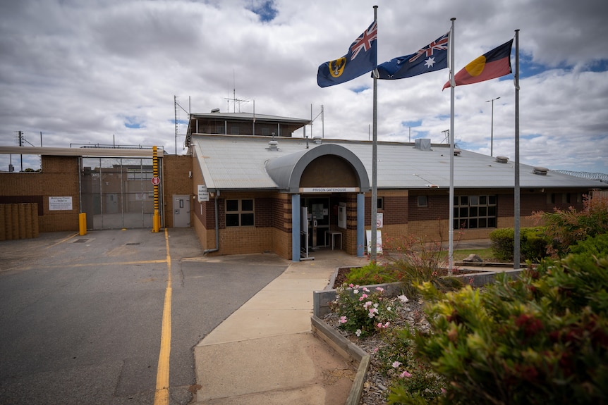 A prison with the South Australian, Australian and Aboriginal flags flying in front of it. To the left the main gated entrance